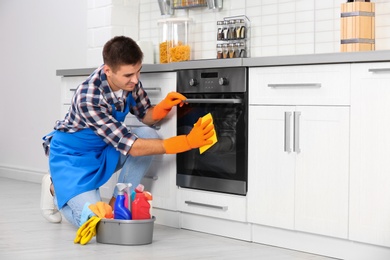 Man cleaning kitchen oven with rag in house