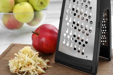 Photo of Grater and fresh ripe apple on wooden board, closeup