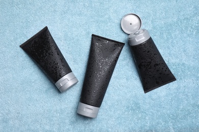 Photo of Black tubes with men's cosmetic products on light blue towel, flat lay