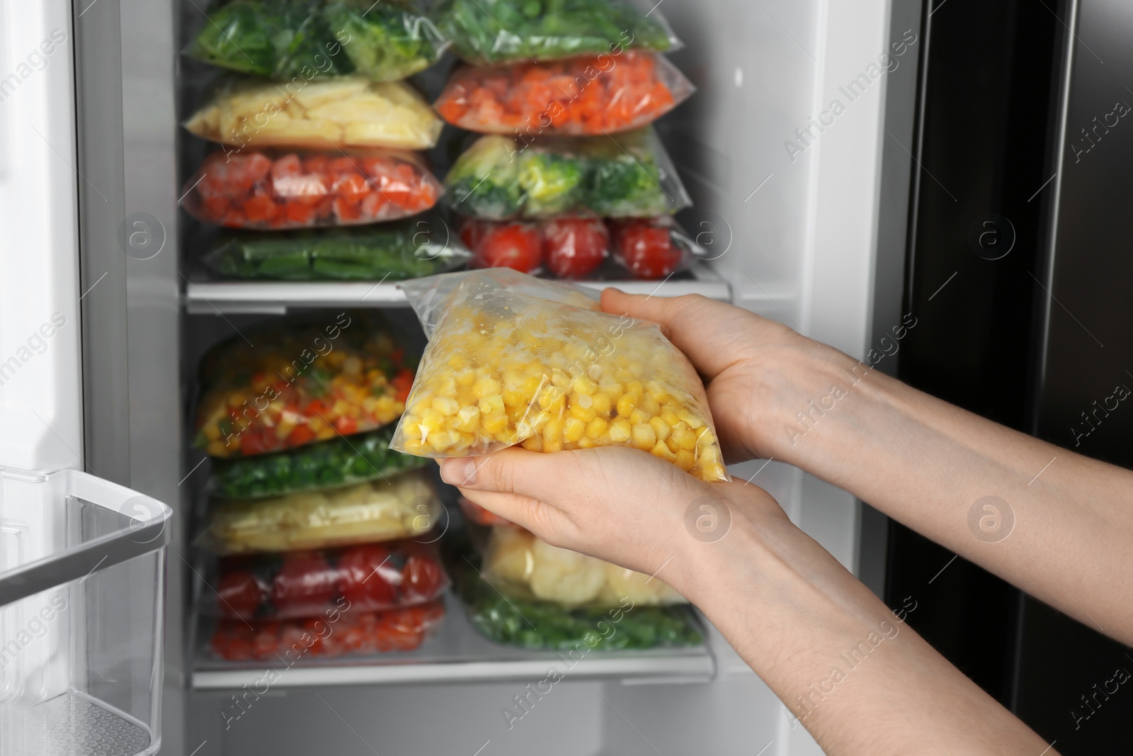 Photo of Woman holding plastic bag with frozen corn near open refrigerator, closeup