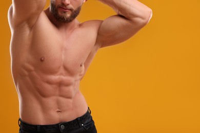 Photo of Muscular man showing abs on orange background, closeup and space for text. Sexy body