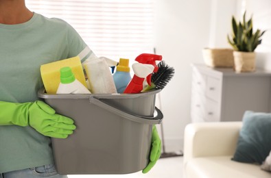 Photo of Woman holding bucket with cleaning supplies in living room, closeup. Space for text