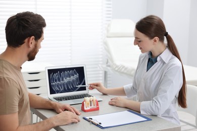 Photo of Doctor showing patient X-ray picture and educational model of dental implant in clinic