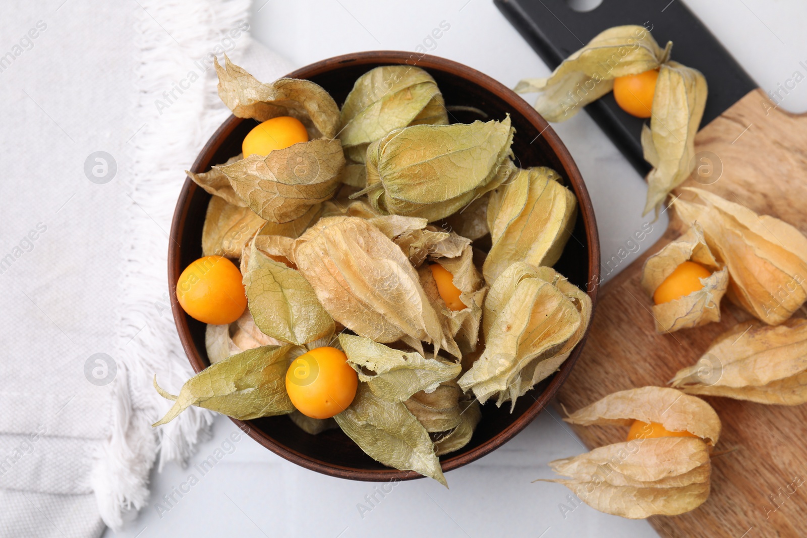 Photo of Ripe physalis fruits with calyxes on white tiled table, top view