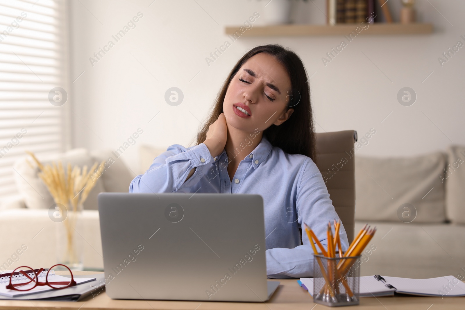 Photo of Young woman suffering from neck pain at table in office