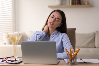 Young woman suffering from neck pain at table in office