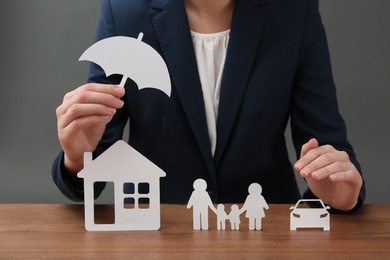 Photo of Woman with cutout paper family, house, car and umbrella at table, closeup. Life insurance concept