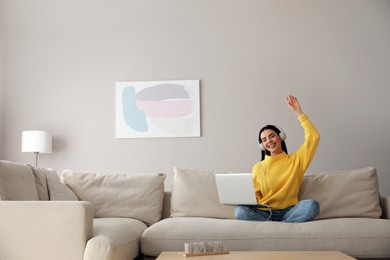 Woman with laptop and headphones sitting on sofa at home