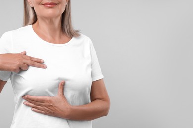 Woman doing breast self-examination on light grey background, closeup. Space for text