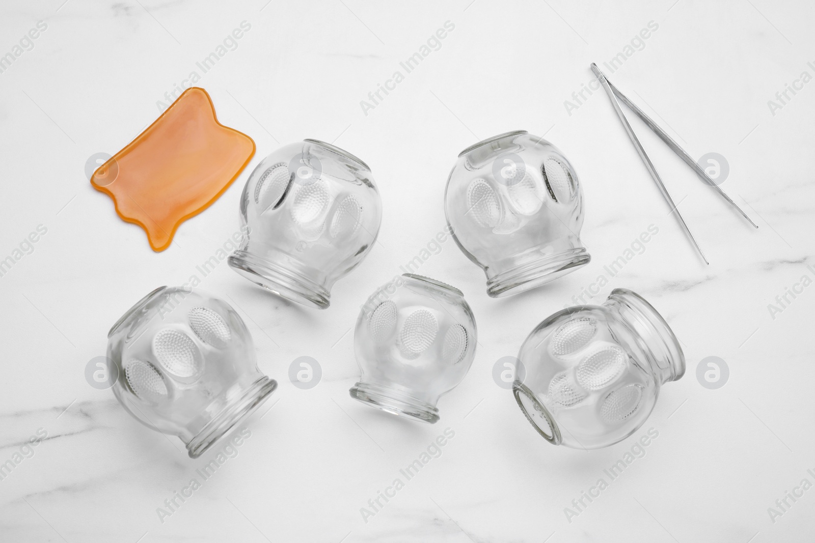 Photo of Glass cups, gua sha and tweezers on white marble table, flat lay. Cupping therapy