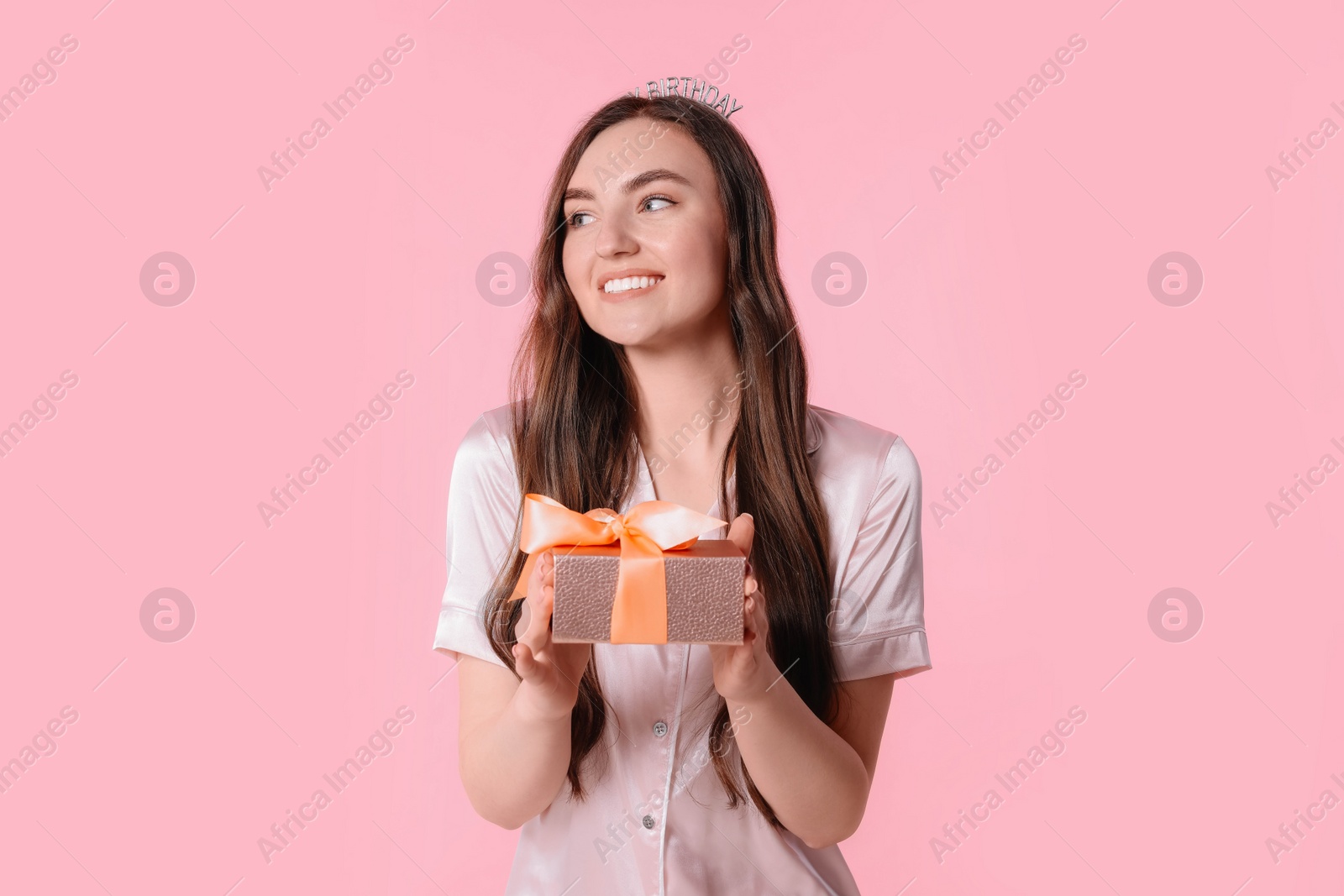 Photo of Beautiful young woman in headband holding gift box on pink background. Happy Birthday