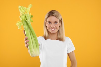 Photo of Happy woman holding fresh green celery bunch on orange background, selective focus