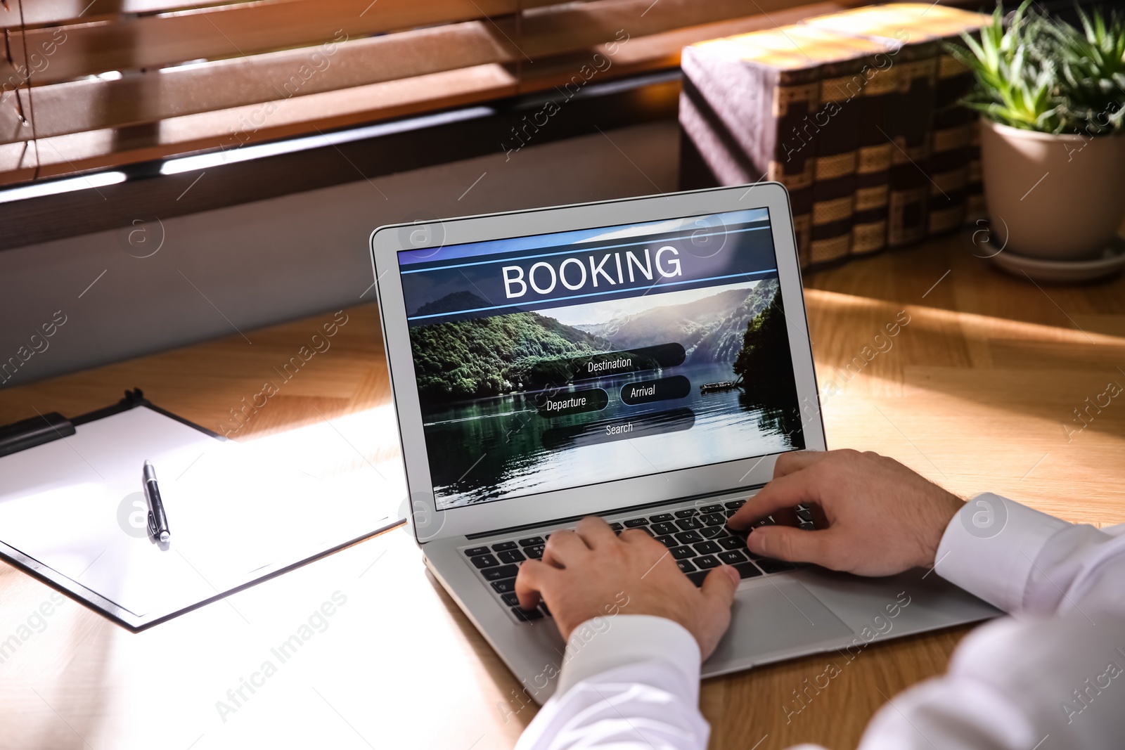 Photo of Man with laptop booking tickets online at wooden table, closeup. Travel agency concept