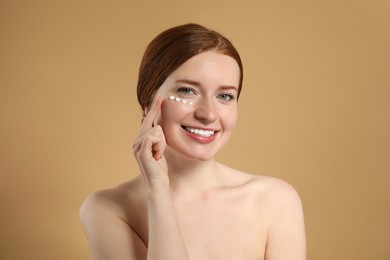 Photo of Smiling woman with freckles and cream on her face against beige background