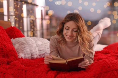 Beautiful young woman with book relaxing on bed at home. Cozy atmosphere