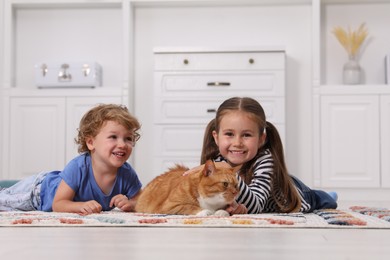Little children and cute ginger cat on carpet at home