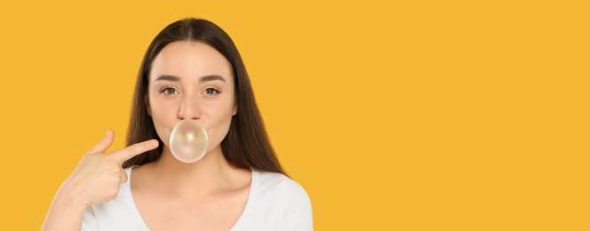 Photo of Beautiful young woman blowing bubble gum on yellow background