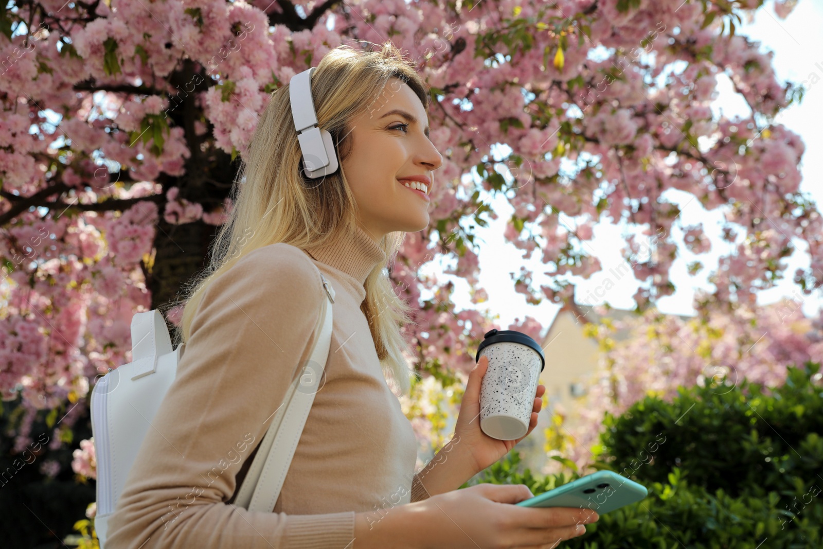 Photo of Happy woman with smartphone and coffee listening to audiobook outdoors on spring day