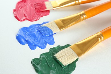 Photo of Brushes with bright paints on white background, closeup