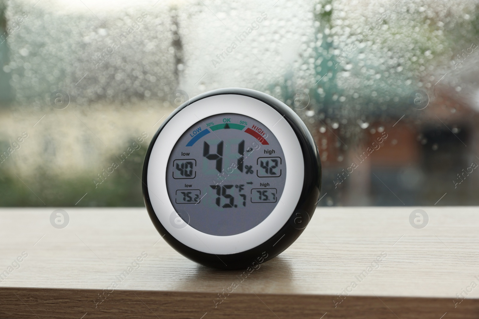 Photo of Digital hygrometer with thermometer near window on rainy day