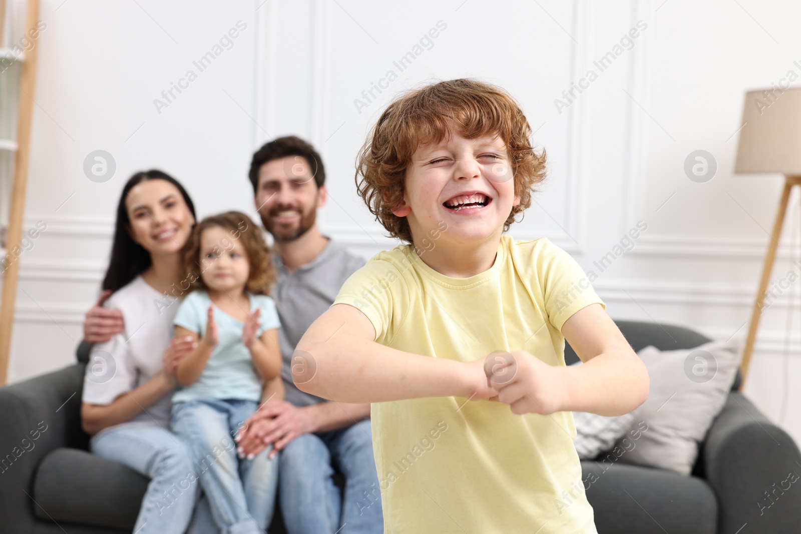 Photo of Happy family having fun at home. Son dancing while his relatives resting on sofa