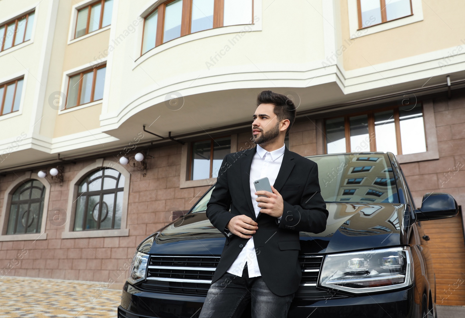 Photo of Handsome young man with smartphone near modern car outdoors