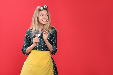 Photo of Young housewife with glass of martini on red background. Space for text