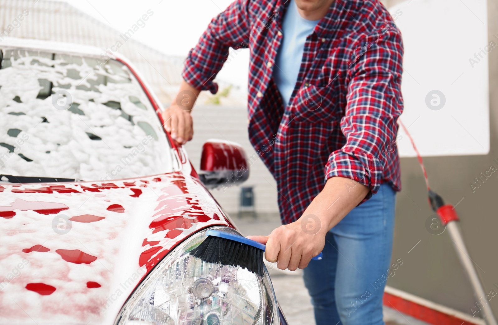 Photo of Young man cleaning vehicle with brush at self-service car wash