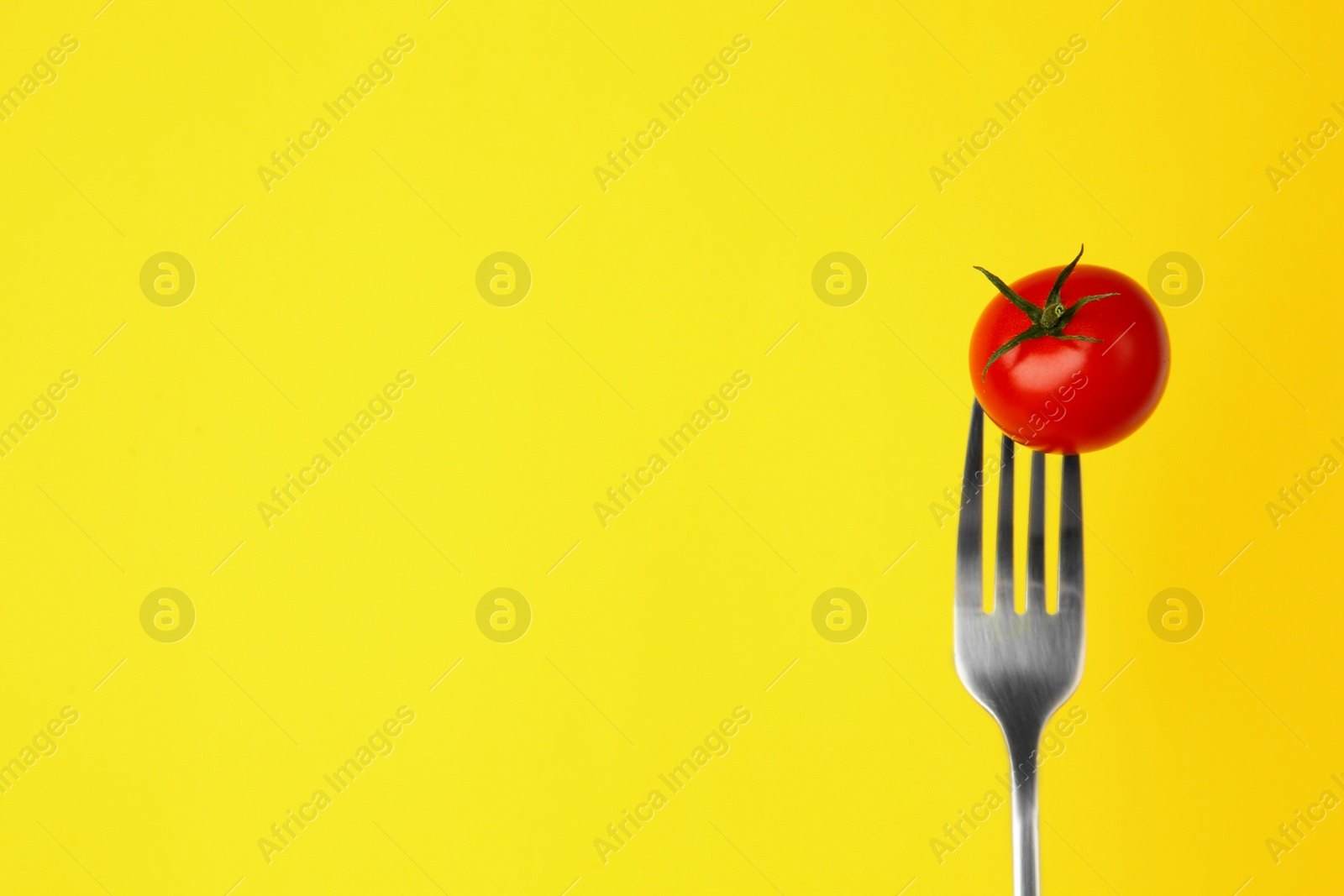 Photo of Fork with cherry tomato on yellow background, space for text