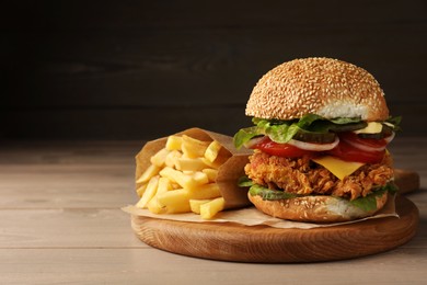 Photo of Delicious burger with crispy chicken patty and french fries on wooden table. Space for text