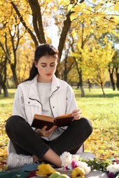 Woman reading book in park on autumn day