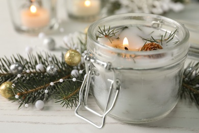 Burning scented conifer candle and Christmas decor on white wooden table, closeup