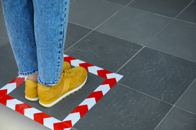 Photo of Woman standing on taped floor marking for social distance, closeup. Coronavirus pandemic