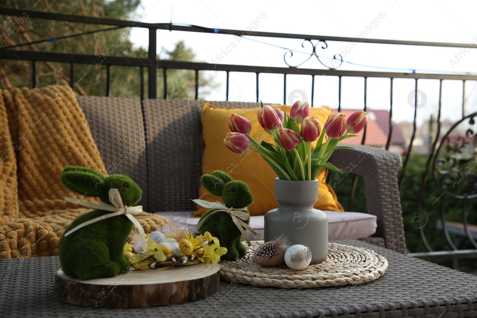 Photo of Terrace with Easter decorations. Bouquet of tulips in vase, bunny figures, decorative nest and eggs on table outdoors