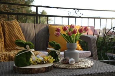 Terrace with Easter decorations. Bouquet of tulips in vase, bunny figures, decorative nest and eggs on table outdoors