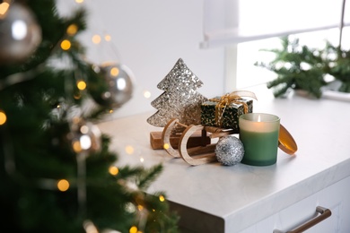 Photo of Toy sleigh with gift box, decorative Christmas tree, candle and ball on white countertop indoors