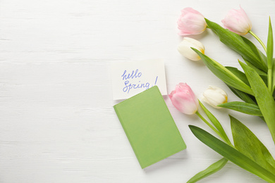 Photo of Card with words HELLO SPRING, notebook and tulips on white wooden table, flat lay. Space for text