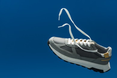 Photo of One stylish grey sneaker in air against blue background, space for text