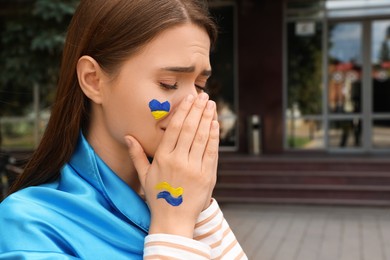 Photo of Sad young Ukrainian woman with clasped hands outdoors. Space for text