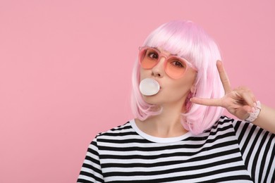 Photo of Beautiful woman in sunglasses blowing bubble gum and gesturing on pink background, space for text