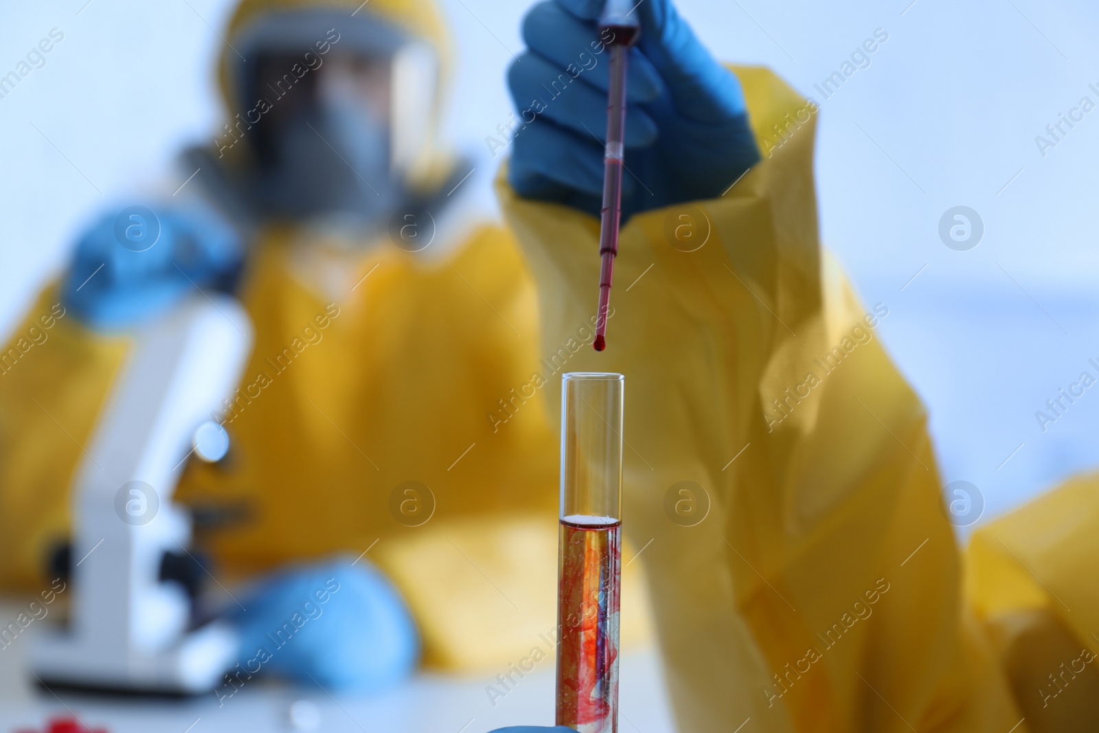 Photo of Scientist in chemical protective suit dripping blood  into test tube at laboratory, closeup. Virus research