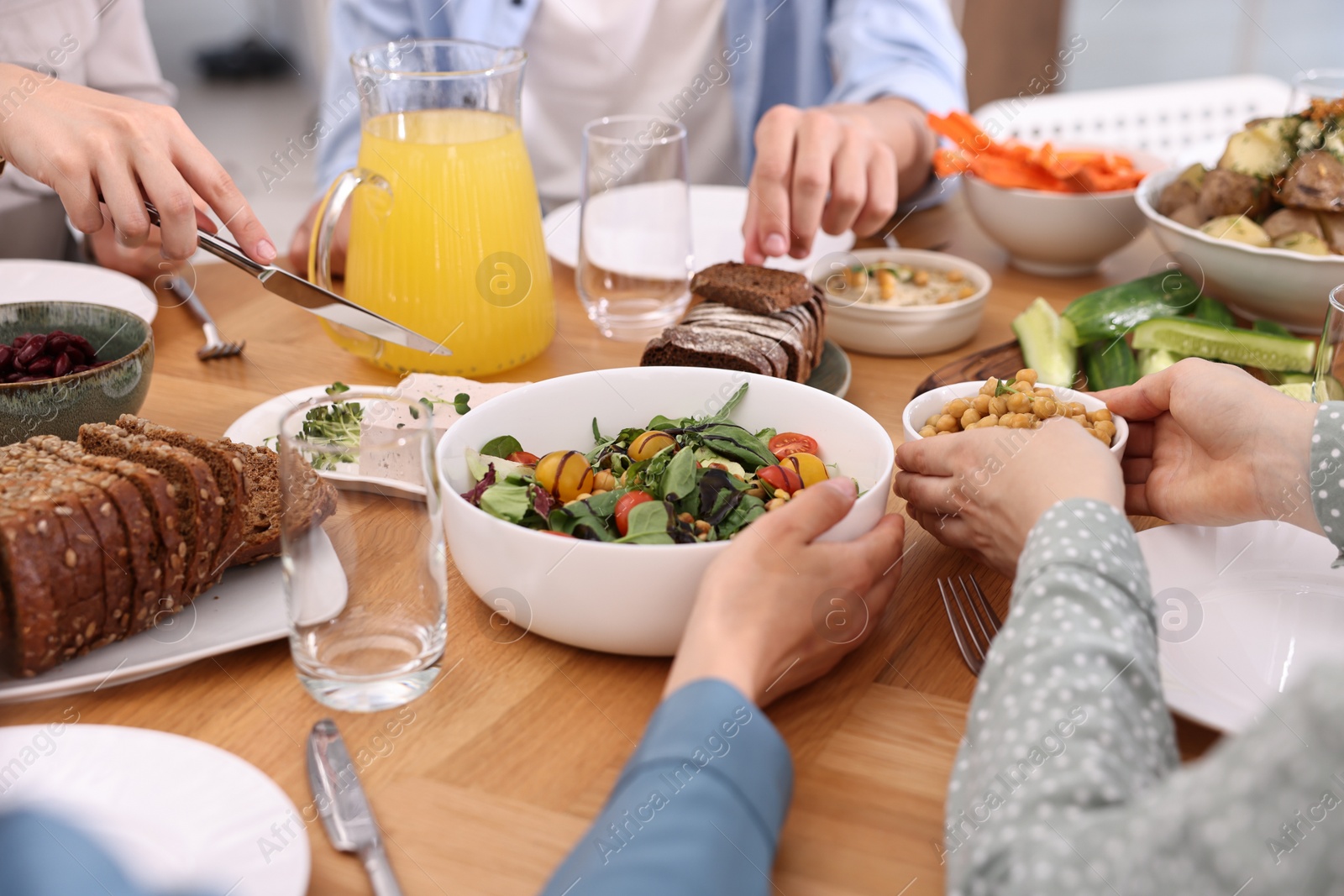 Photo of Friends eating vegetarian food at wooden table indoors, closeup