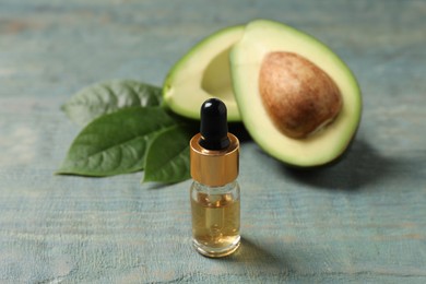 Photo of Bottle of essential oil and avocado on light blue wooden table