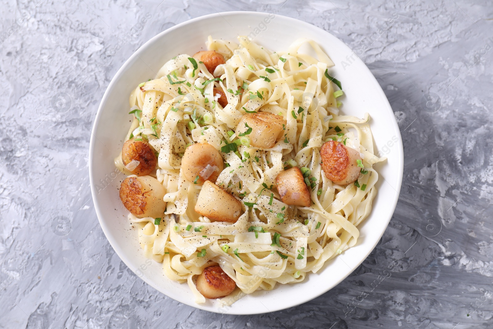 Photo of Delicious scallop pasta with spices in bowl on gray textured table, top view