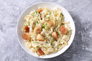 Photo of Delicious scallop pasta with spices in bowl on gray textured table, top view