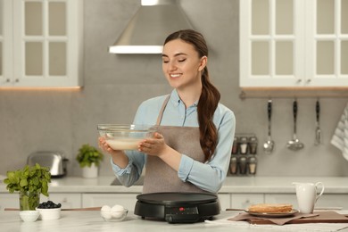 Happy woman with dough for crepes at white marble table in kitchen