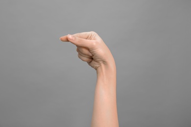 Woman showing G letter on grey background, closeup. Sign language