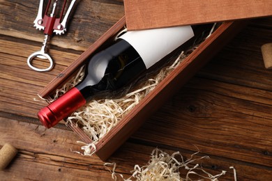 Photo of Box with wine bottle, corkscrew and corks on wooden table, flat lay