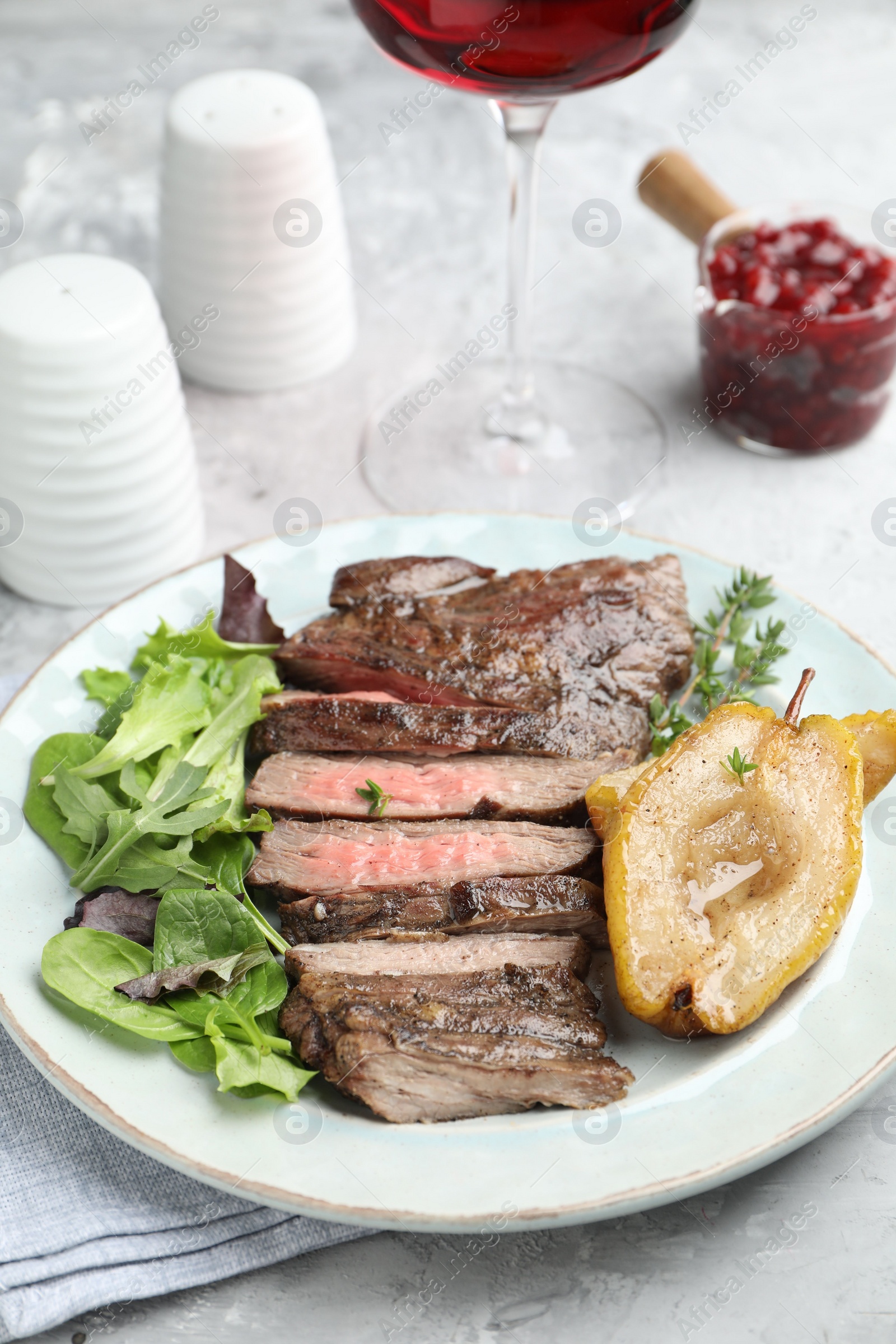 Photo of Delicious roasted beef meat, caramelized pear and greens served on light table