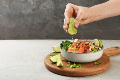 Photo of Woman squeezing lime juice into bowl of delicious ramen with shrimps at light textured table, closeup and space for text. Noodle soup